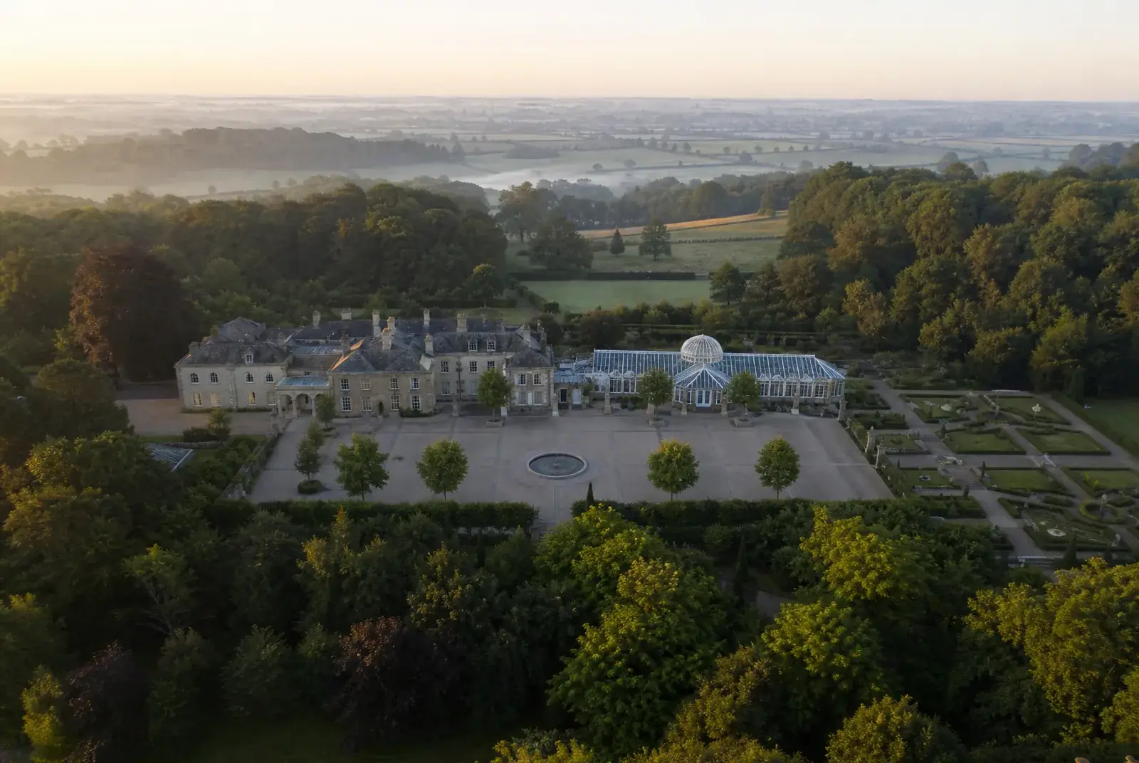 Domaine de réception vu du ciel aux premières lueurs, sa cour pavée, son orangerie et ses jardins encore déserts.
