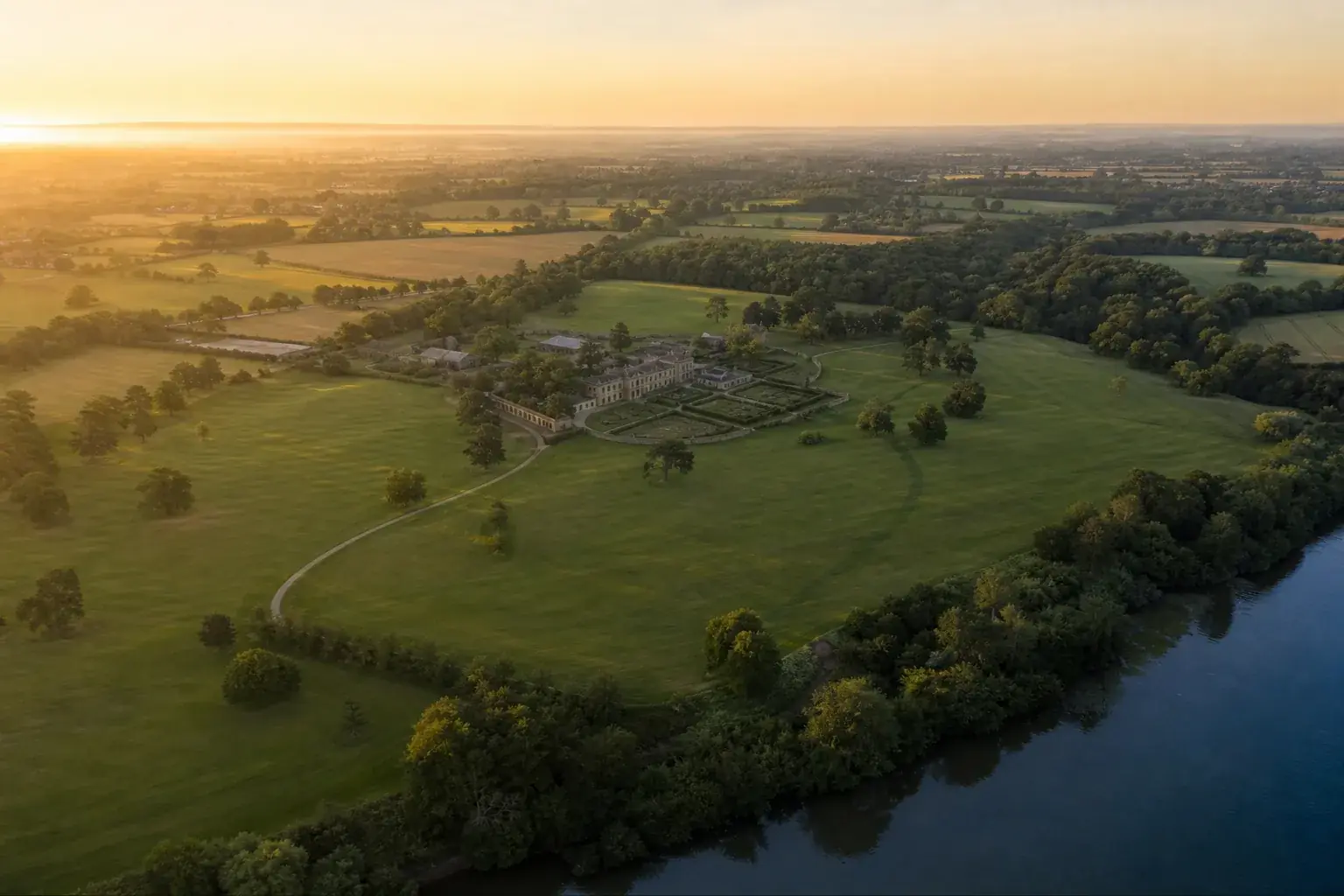 Grand domaine vu du ciel au lever du jour, ses bâtiments groupés au centre et ses terres s’étendant tout autour.