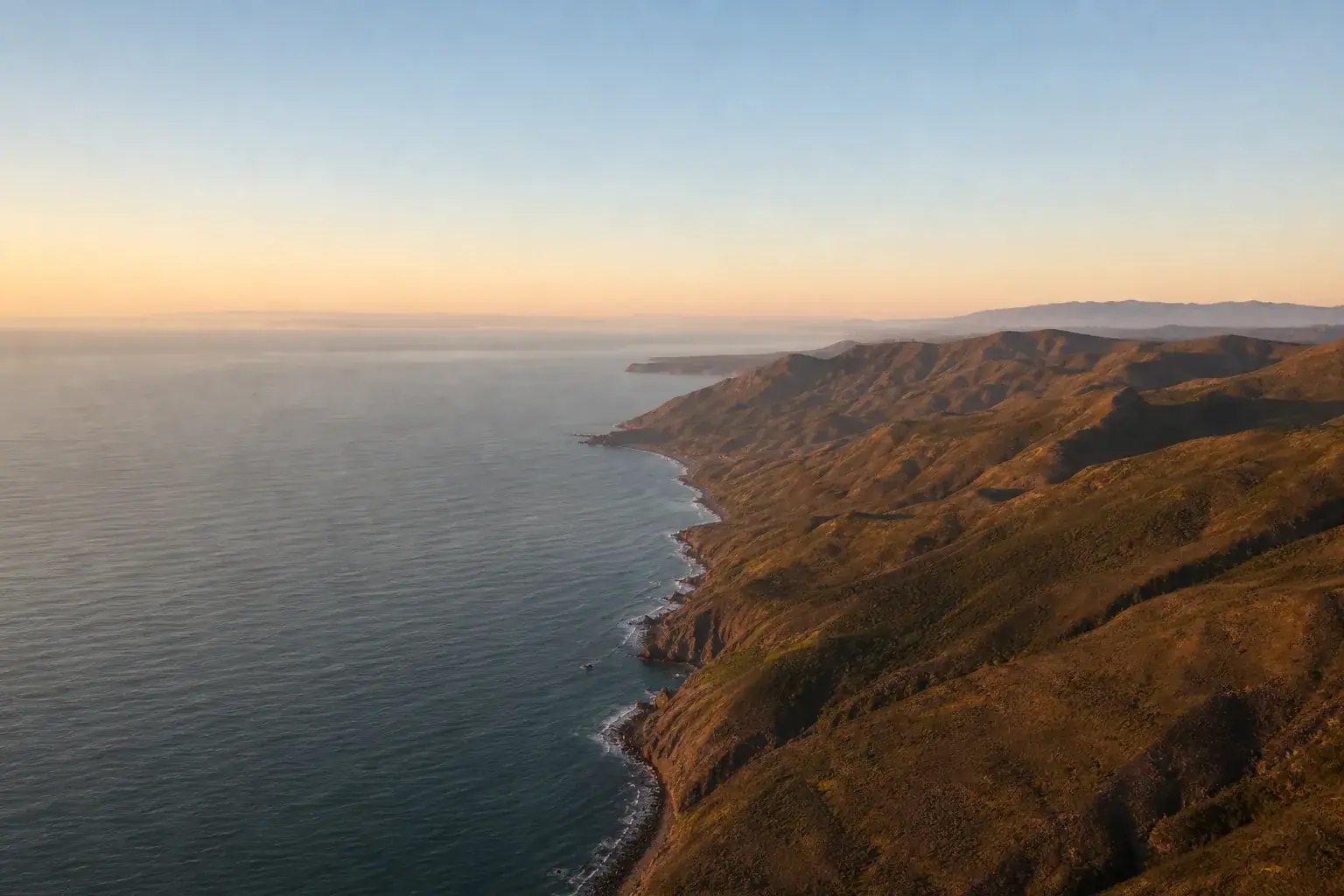Littoral vu de haute altitude au lever du jour, la lumière rasante détachant chaque relief de la côte.