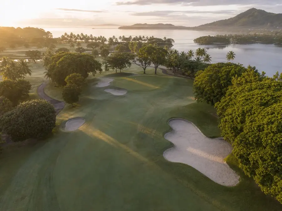 Fairway de golf serpentant entre les bunkers vers un green, à la lumière du matin.