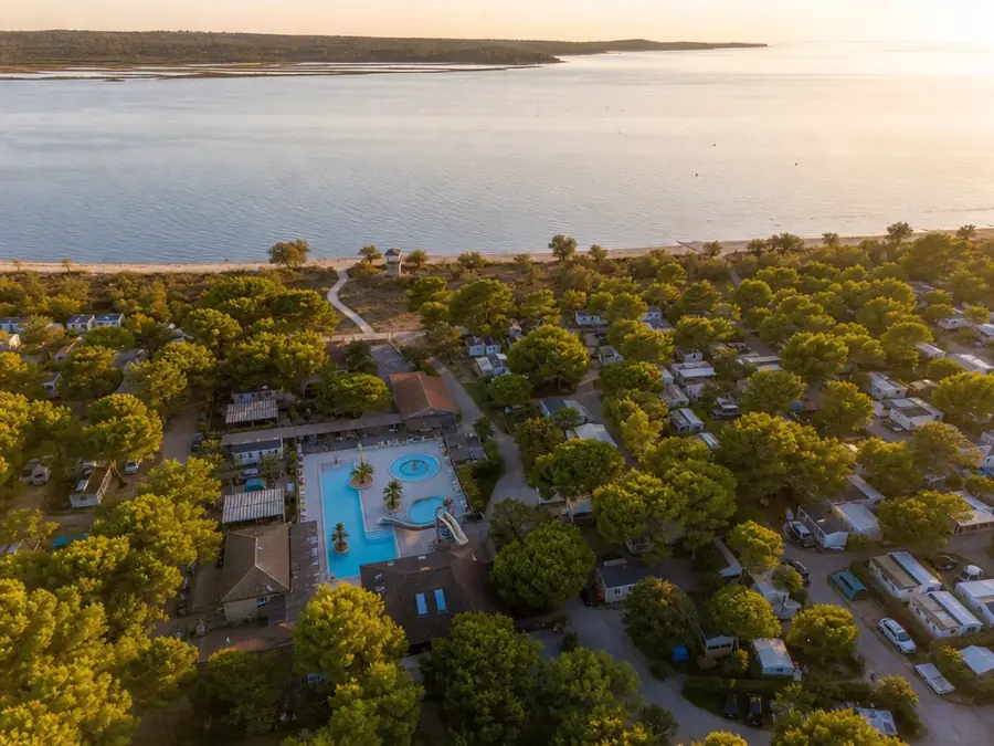 Camping en bord de mer vu du ciel : emplacements, pins, piscine et accès plage.