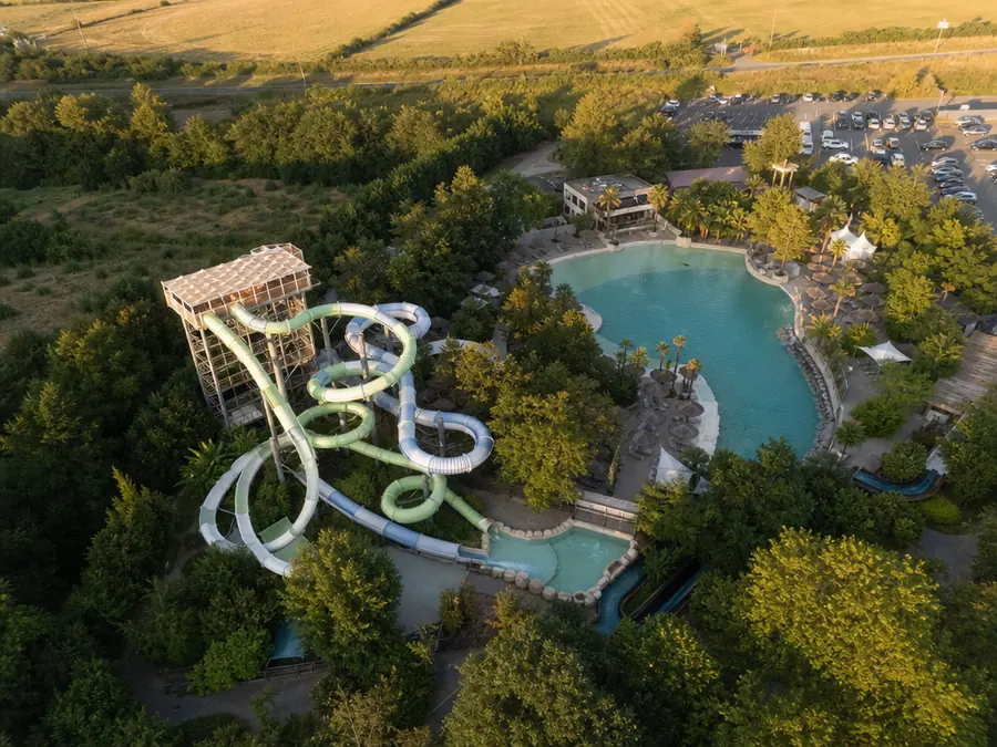 Parc de loisirs vu du ciel : toboggans aquatiques et lagon de baignade entourés de bois.